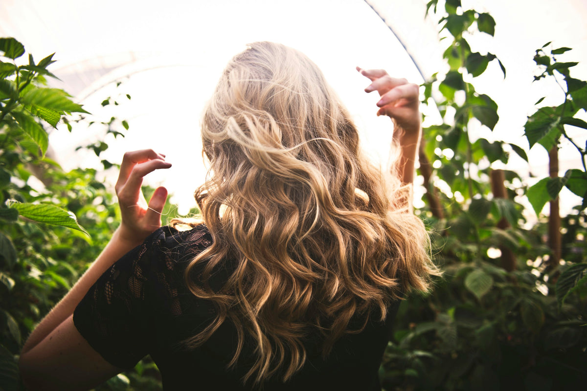 Woman with long wavy hair seen from behind, among green leaves